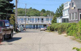 Quiet residential street with parked cars, houses, and a two-story motel in the background.