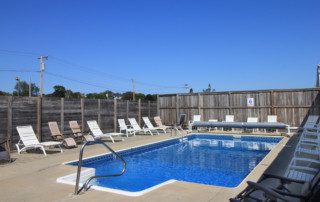 Outdoor pool with lounge chairs and wooden fencing under a clear blue sky.