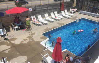 Outdoor pool area with lounge chairs, umbrellas, and people swimming and relaxing.