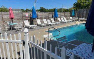 Outdoor swimming pool area with lounge chairs, umbrellas, and a white picket fence.