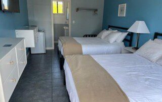 Cozy hotel room with two beds, blue accent wall, mini-fridge, and tiled flooring.