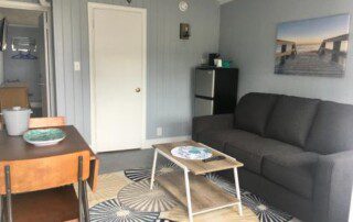 A small living area with a gray couch, a wooden coffee table, and a dining table set.