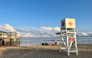 A sunny beach scene with a lifeguard chair, people relaxing, and ocean waves nearby.