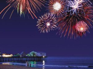 Fireworks over ocean pier at night.